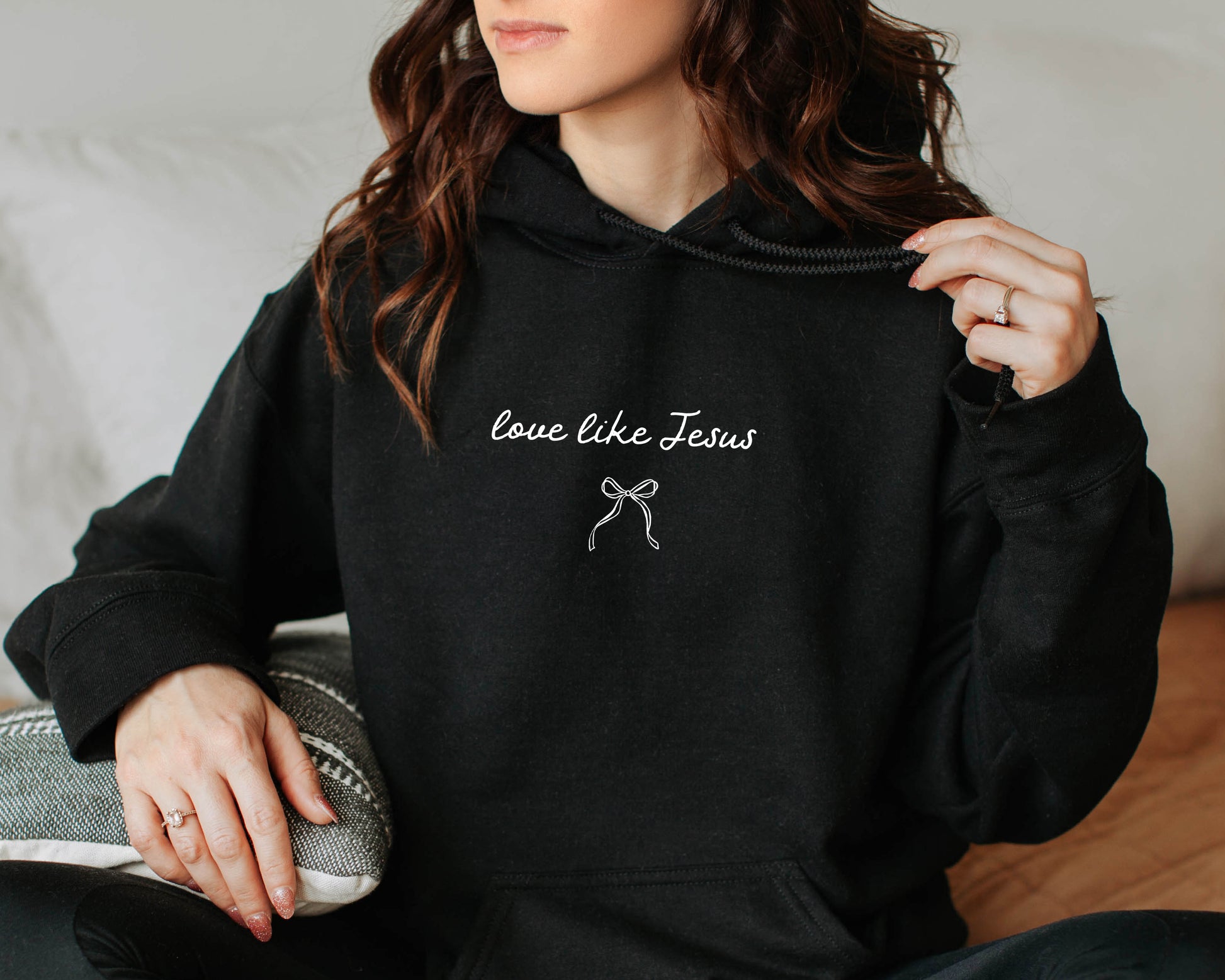 Person wearing a black hoodie with 'love like Jesus' text and a bow graphic.