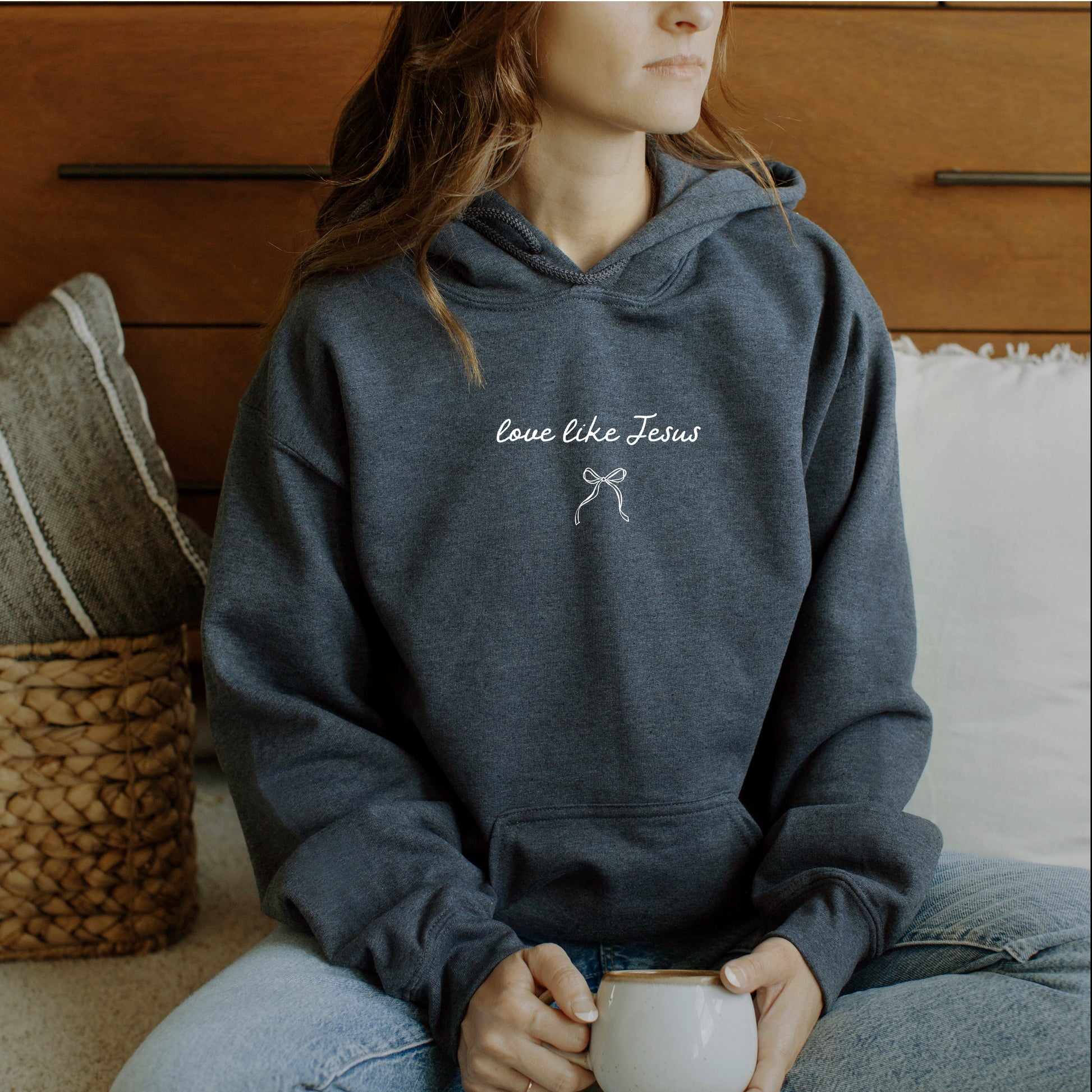 Person wearing a hoodie with 'love like Jesus' text sitting on a couch.