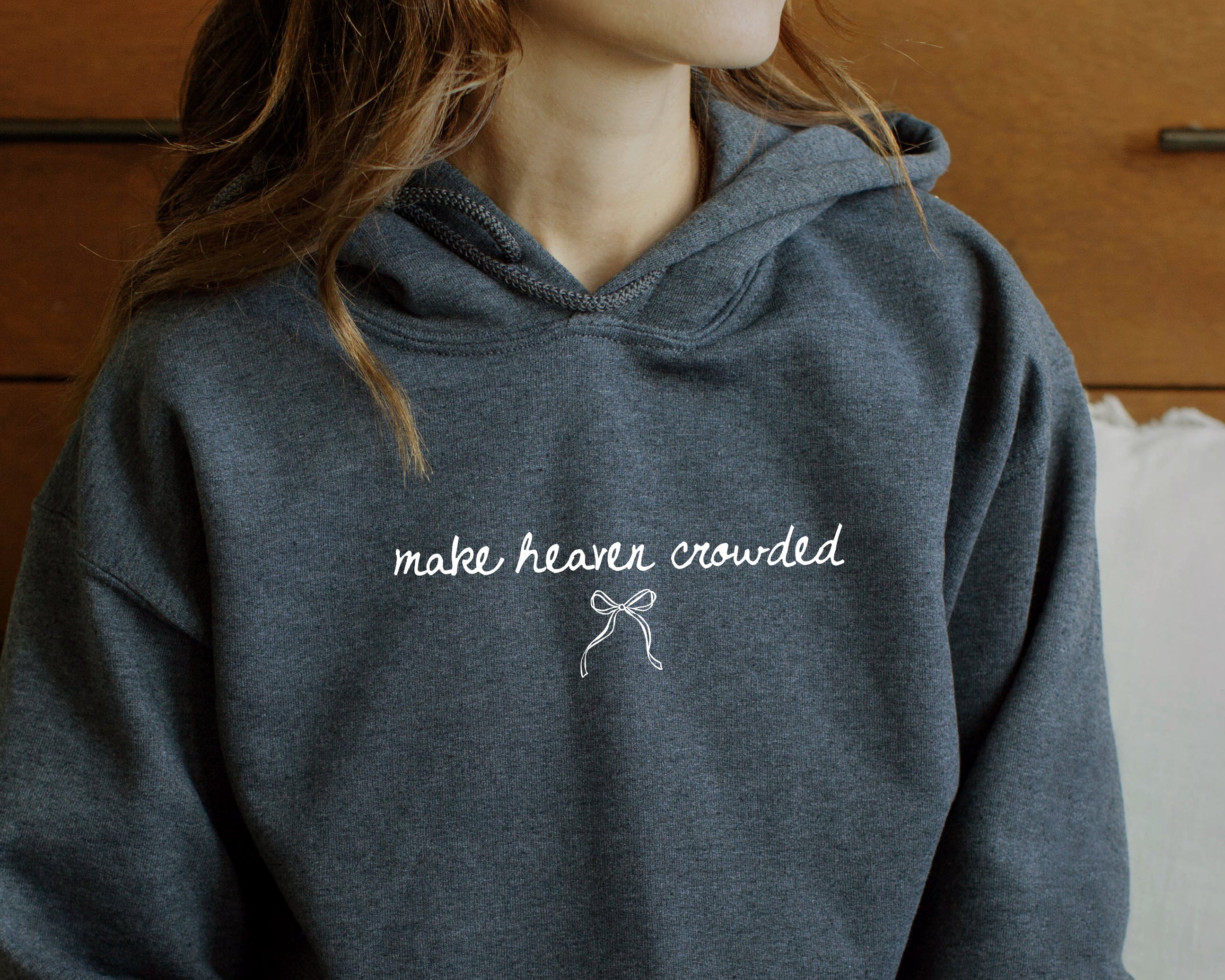 Person wearing a dark gray hoodie with 'make heaven crowded' text and a bow graphic.
